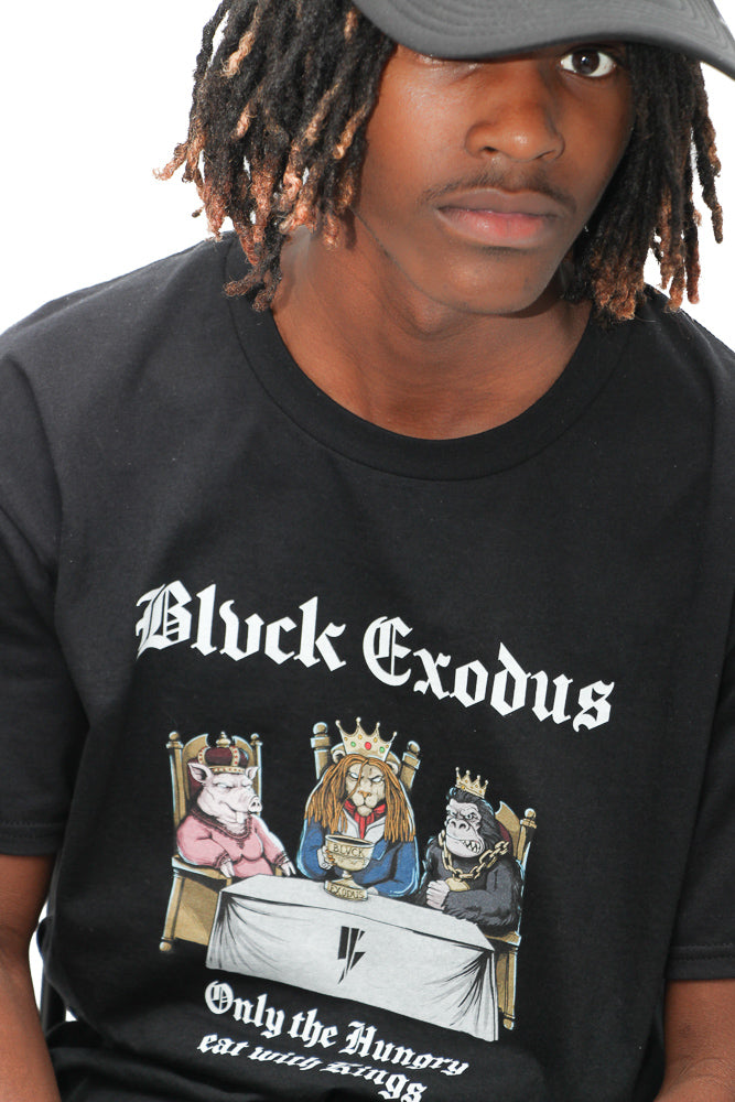 Black male wearing black short-sleeve t-shirt featuring a vintage-inspired graphic of animals sitting at a table with the text "Only the Hungry Eat with Kings" in a bold, gothic font, and the Blvck Exodus logo.
