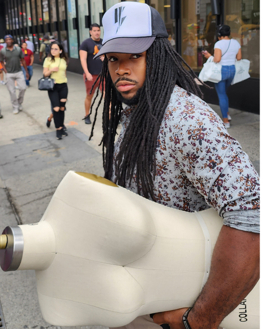 A man with locs and a trucker hat on carrying a mannequin 