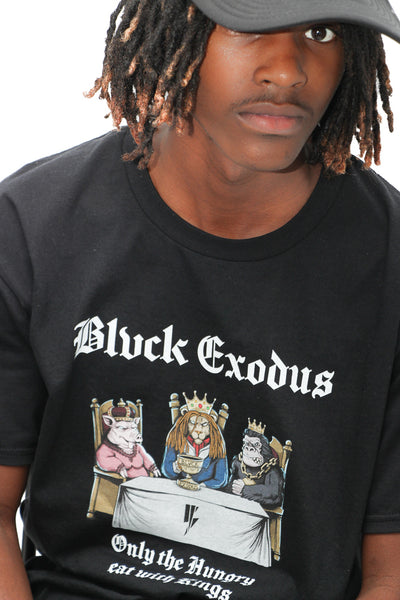 Black male wearing black short-sleeve t-shirt featuring a vintage-inspired graphic of animals sitting at a table with the text "Only the Hungry Eat with Kings" in a bold, gothic font, and the Blvck Exodus logo.